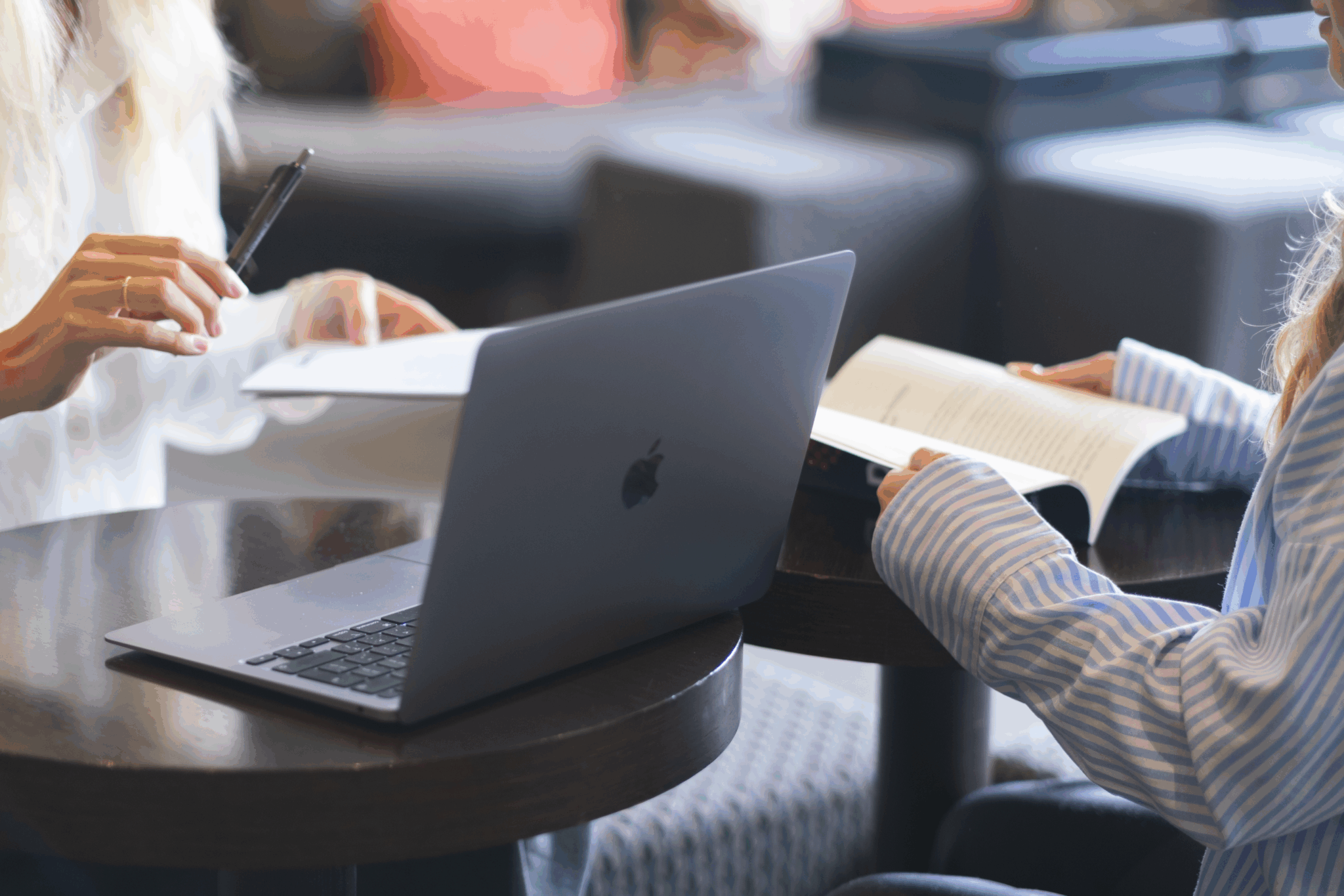 Two people collaborating together; one works at a laptop and one reads from a book.