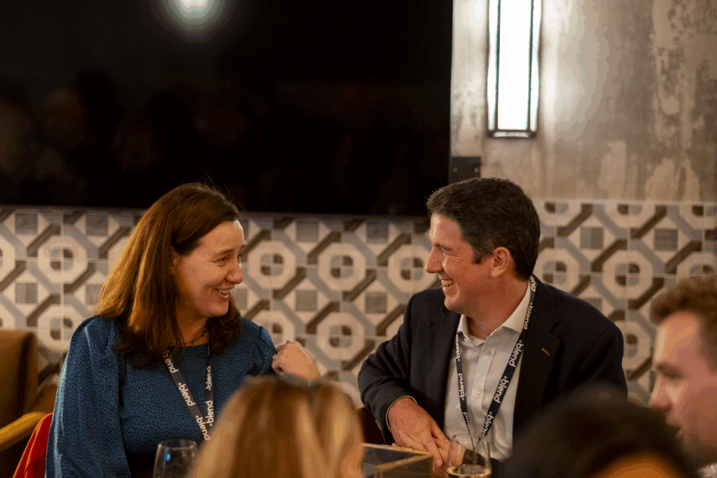 Two C-suite professionals talk at a Blend community networking event, wearing Blend branded lanyards. They are seated.