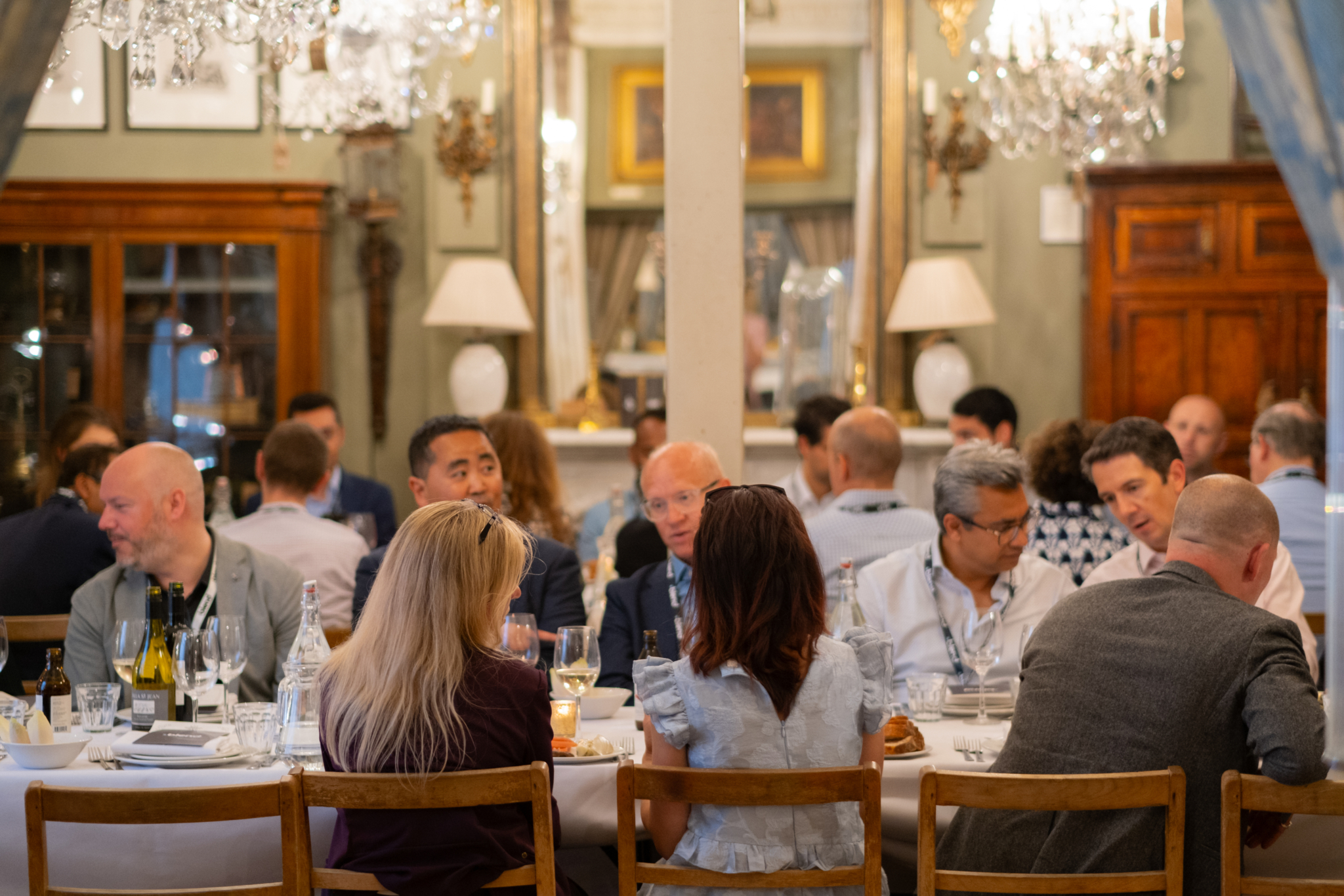 A large group of C-suite professionals engage in conversation at a Blend community networking event. They wear Blend lanyards and are seated at a long dining table.