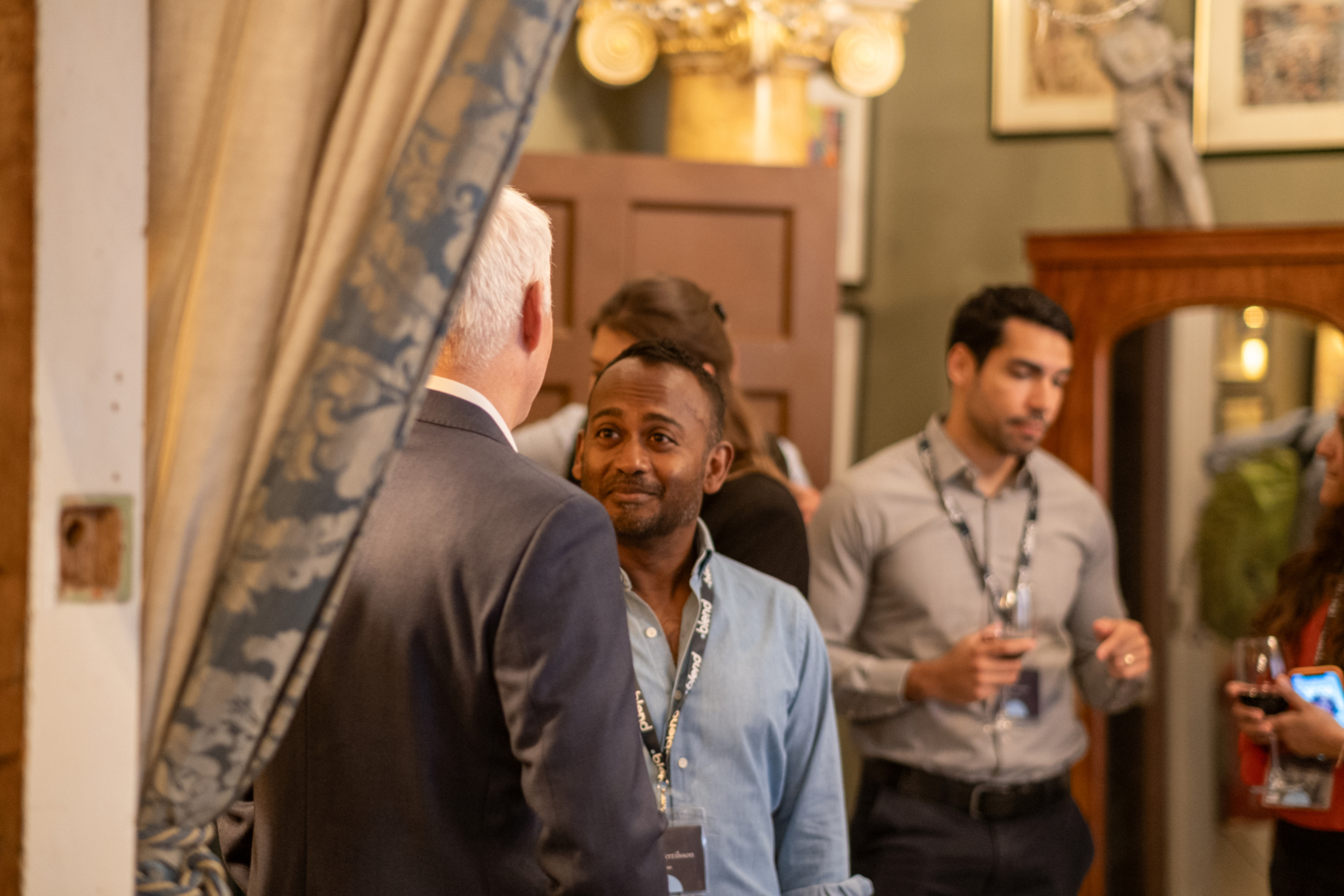 C-suite professionals engage in conversation at a Blend community networking event. They wear Blend lanyards.