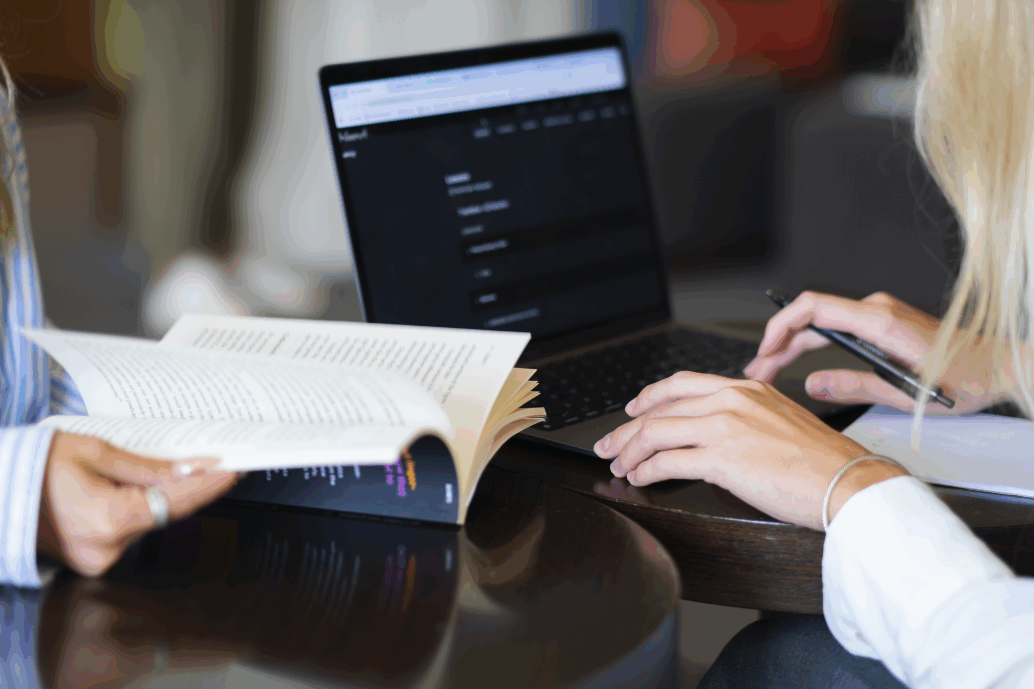 Two people collaborating together; one works at a laptop and one reads from a book.