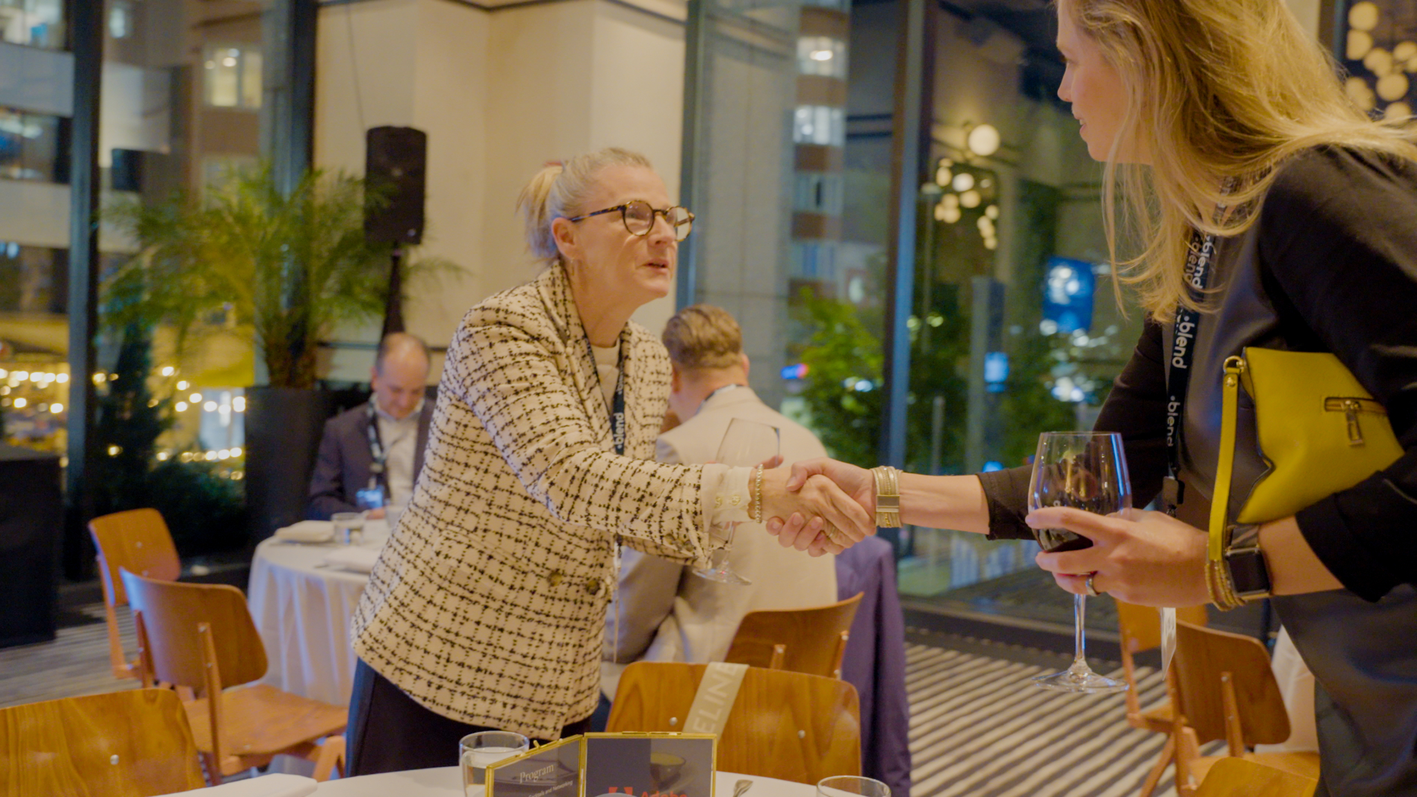 Two C-suite professionals introduce themselves to each other and shake hands at a Blend community networking event. The both wear Blend branded lanyards.